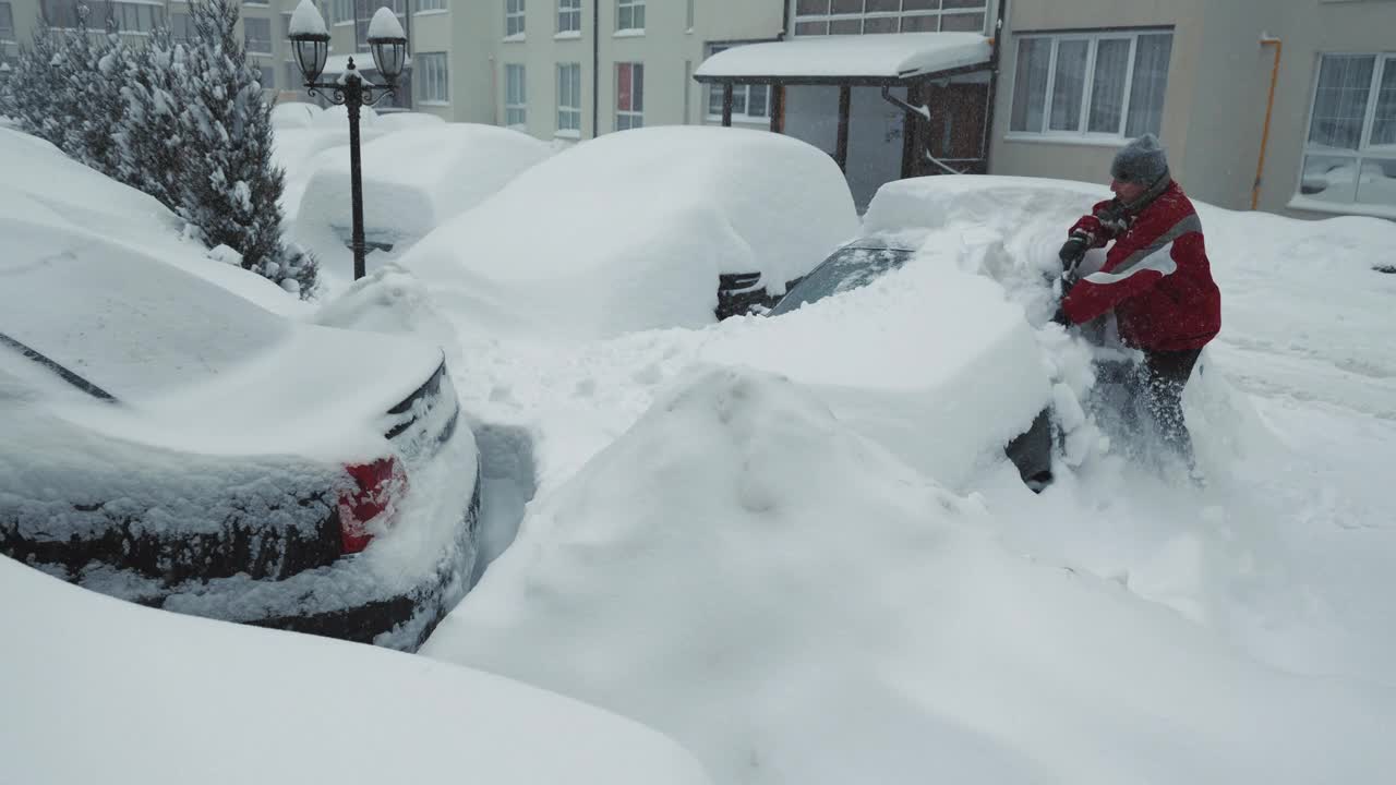 雪堆和风暴。一名男子正在清理一辆被雪覆盖的汽车。大雪。司机背着背包，拿着刷子站在停车场上清理车上的积雪视频素材