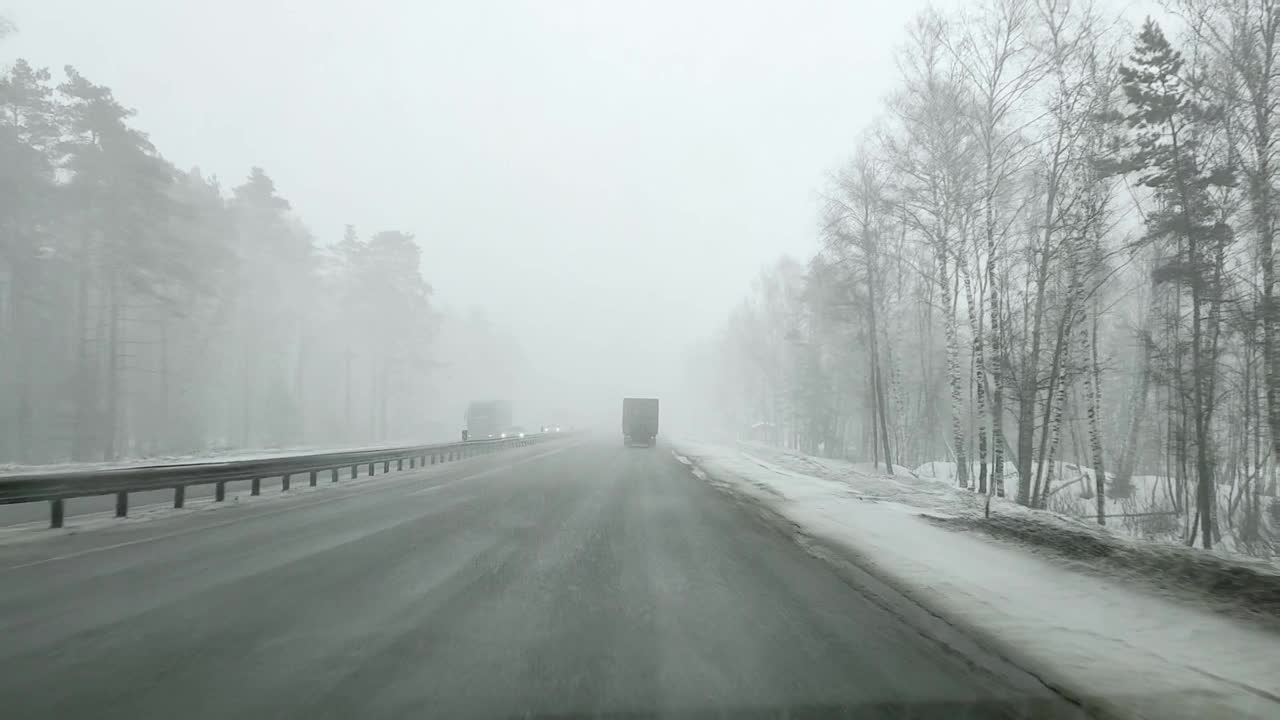 在大雪纷飞的冬天，通过高速公路上一辆汽车的挡风玻璃和一辆超车的卡车视频素材