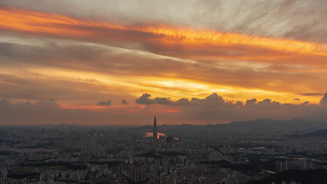 从首尔松坡区南汉山城看日落时，蚕室区乐天世界大厦周围的市中心云朵飘动的夜景视频素材