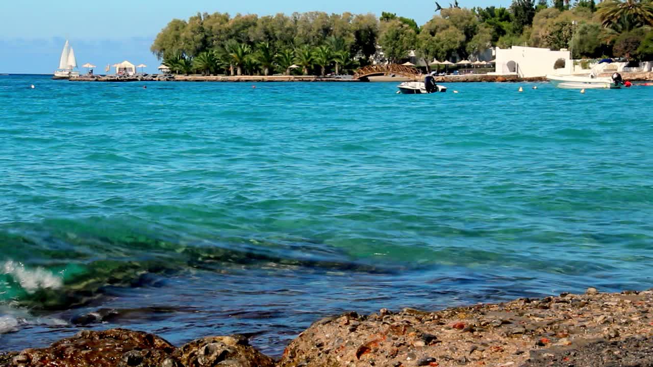 温暖的海岸在壮丽的蔚蓝海湾，小船和快艇在波浪中摇摆，一艘游艇和一艘轮船在远处航行视频素材