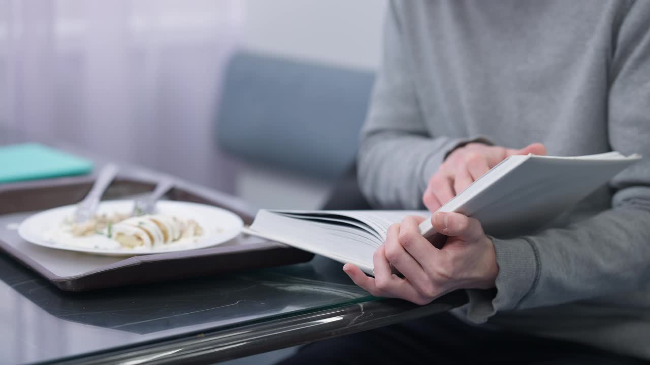 一名不知名的白人年轻人坐在餐厅的桌子旁看书，吃着卷饼。男聪明天才学生在自助餐厅学习和用餐视频素材