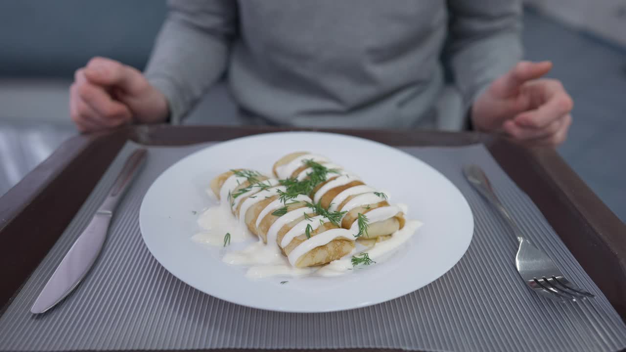 美味的油炸甜煎饼，盘子上有装饰，不认识的人在搓手，拿着刀叉切甜点。年轻的白人男学生在餐厅食堂用餐视频素材