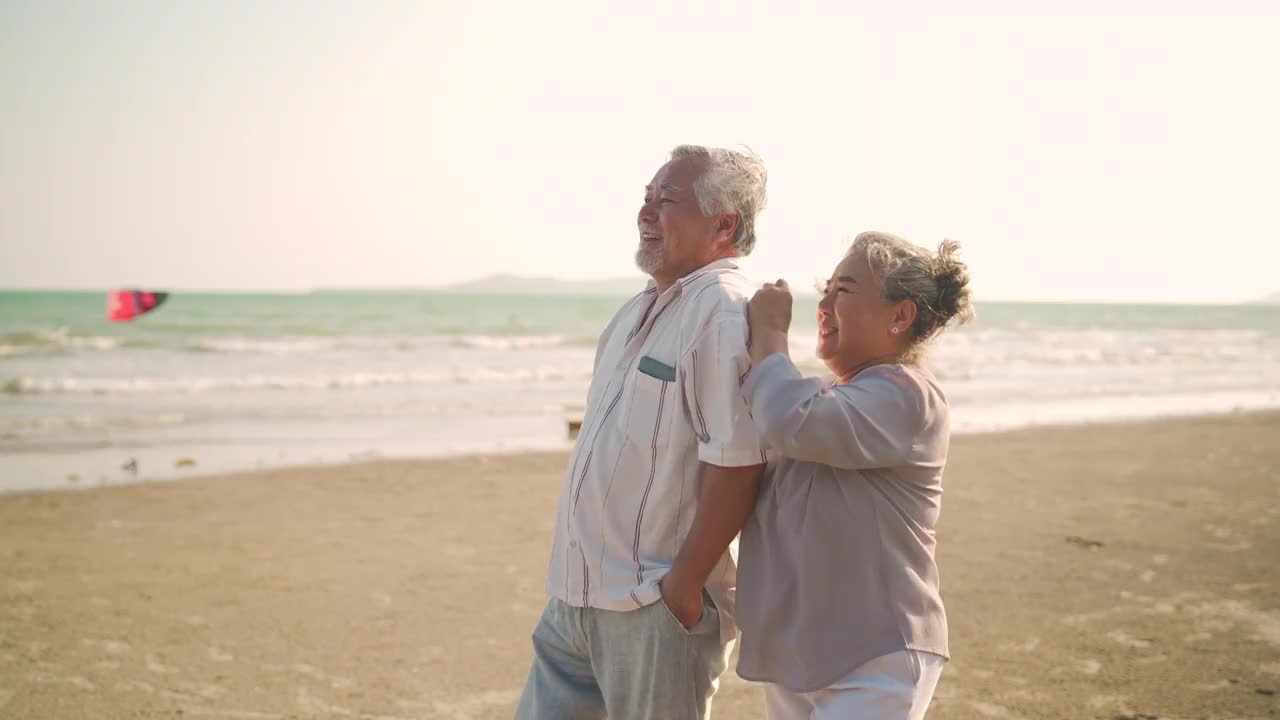 4K亚洲老年夫妇在夏日日落的海滩上享受浪漫的假期，翩翩起舞视频素材