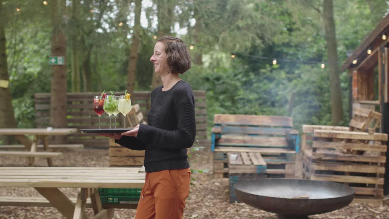 在户外餐馆里，女服务员为坐在桌子旁的四个年轻朋友端饮料视频素材