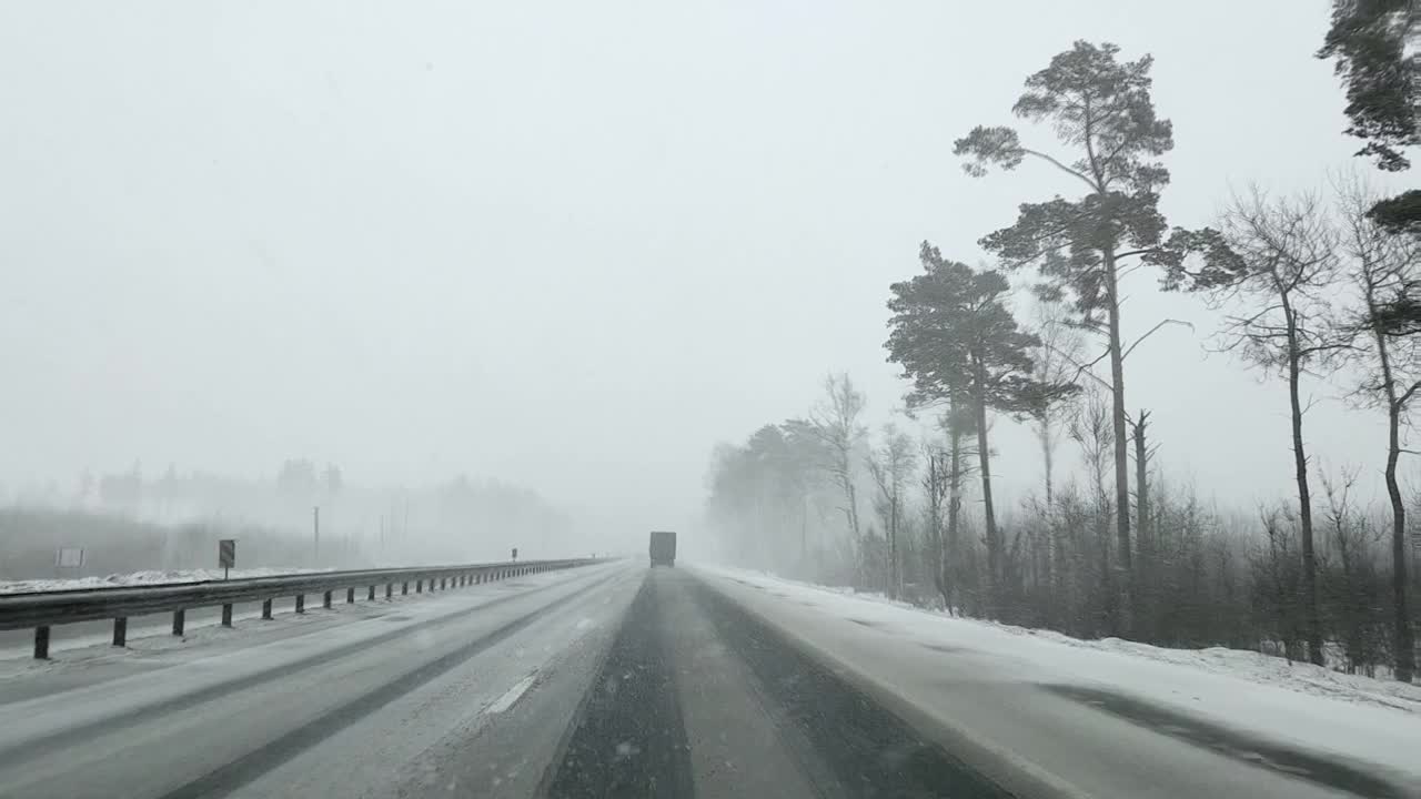 在大雪纷飞的冬天，通过高速公路上的汽车和卡车的挡风玻璃观看视频素材