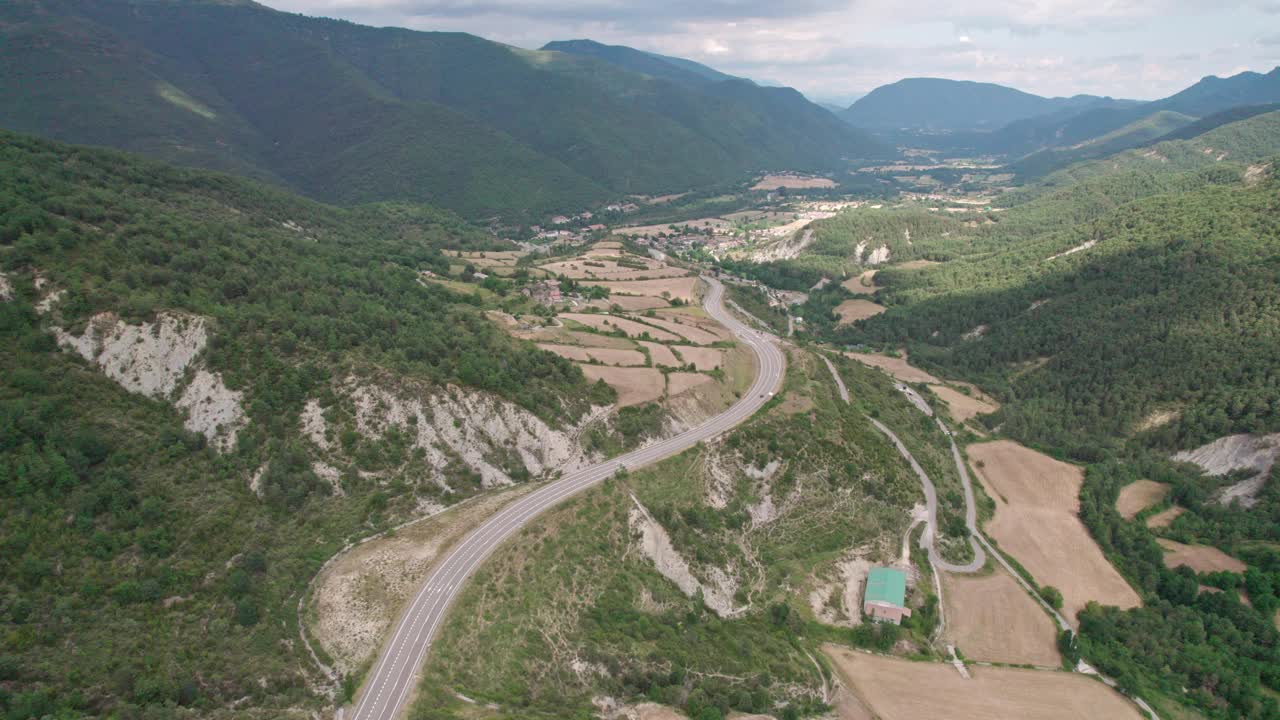 美丽的无人机视野的沥青公路在高山上。山脉消失在天空中，天空有些许阴云，但山峰被阳光照亮。视频素材