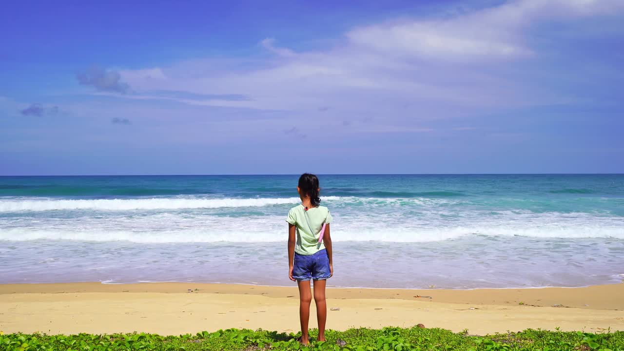 快乐的年轻女孩在海滩上举起了手在卡隆海滩神奇的海热带海滩夏天阳光灿烂的日子美丽的蓝天在好天气的日子女孩站在海岸线上看海浪视频素材