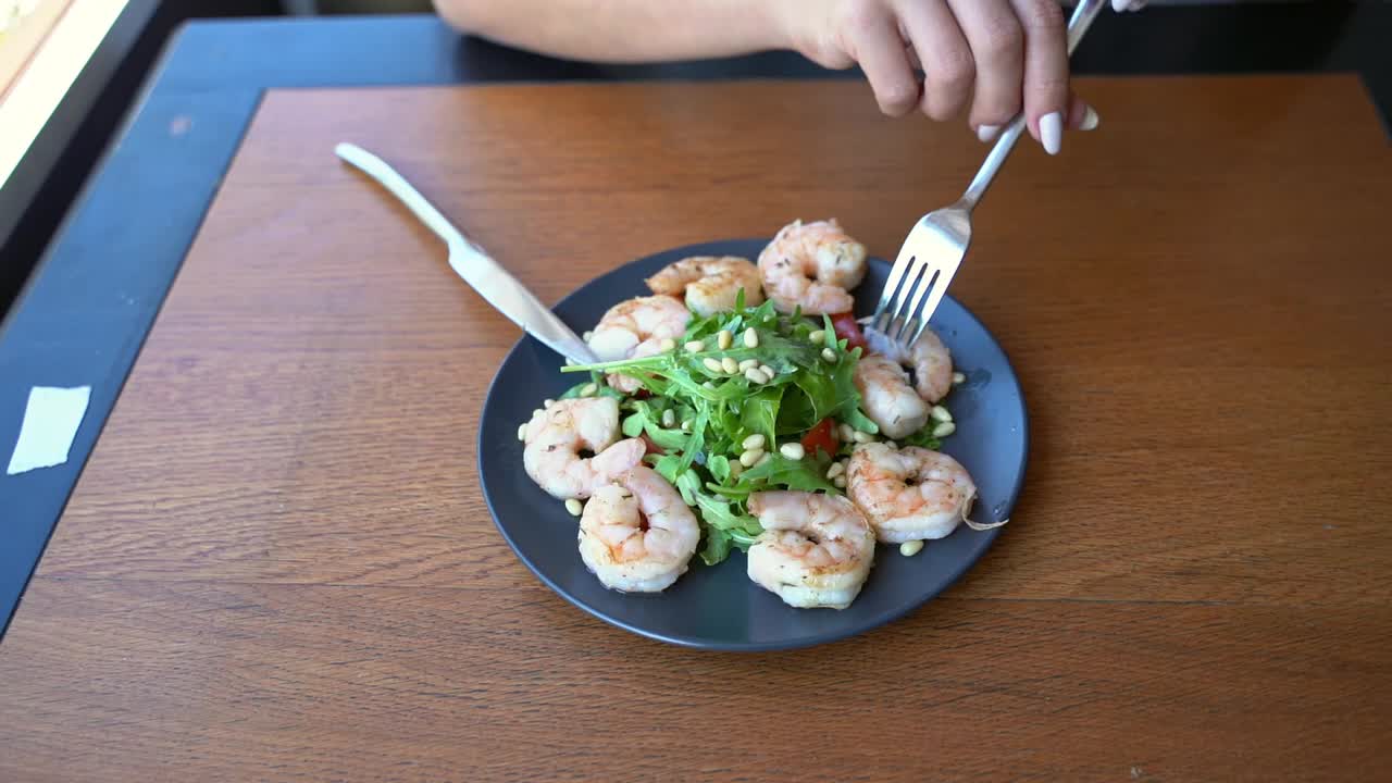 年轻女子在餐厅吃虾沙拉。健康食品的概念。叉,刀视频素材