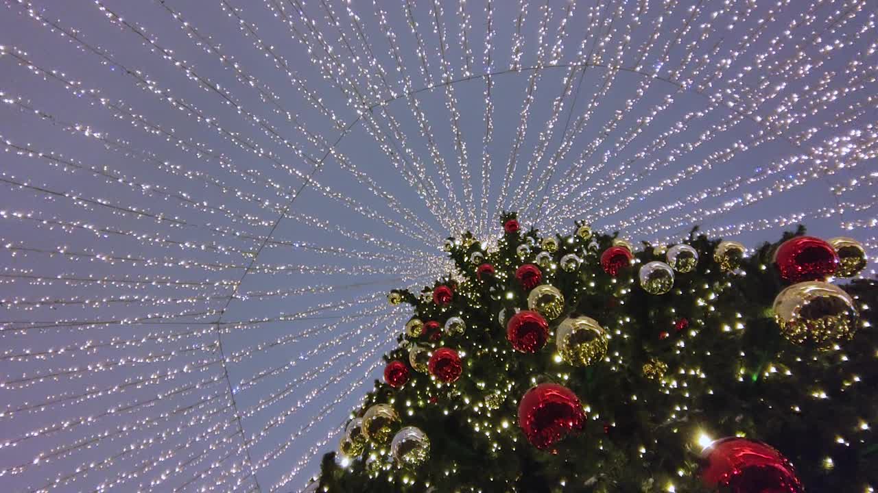 在夜空的映衬下，一棵圣诞树上挂着红色和金色的球，还有一个闪闪发光的花环视频下载