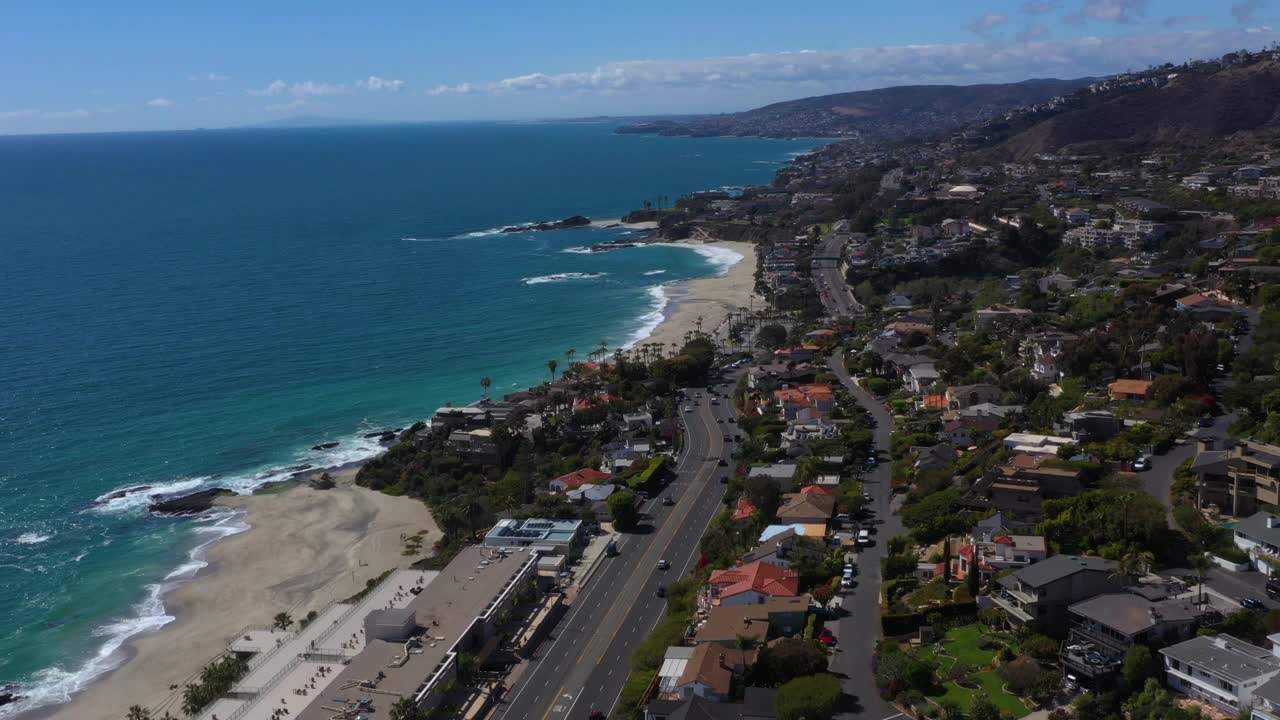 在一个阳光明媚的日子，无人机在沿太平洋海岸1号公路的一个海岸海滩社区上空飞行。视频素材