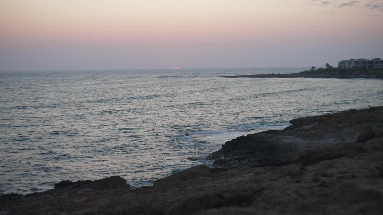 宽镜头日落在灰色蓝色地中海与泡沫波浪翻滚的海岸在慢动作。黄昏时室外退潮。风景如画的黄昏。视频素材