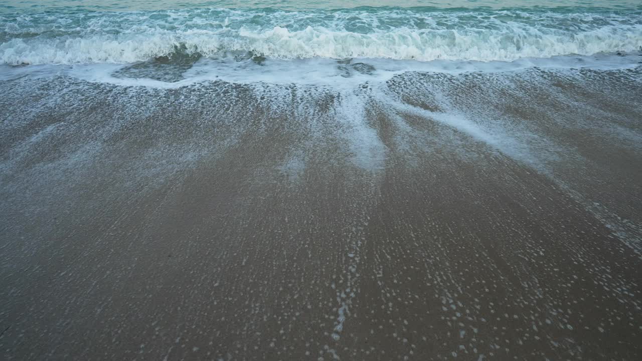 蓝绿色的地中海海浪缓慢地在沙滩上翻滚。美丽、干净、清澈的泡沫水溅在户外的沙子上。旅游与宁静的概念。视频素材