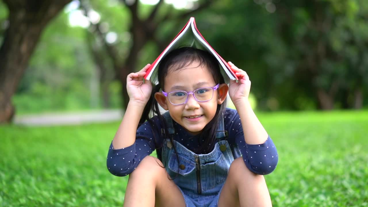 快乐的亚洲小女孩和书在花园里视频下载