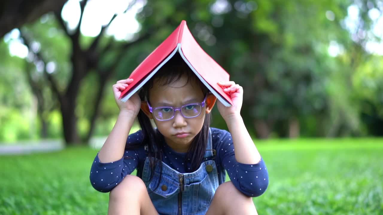 慢动作亚洲小女孩头上拿着书在花园里视频素材