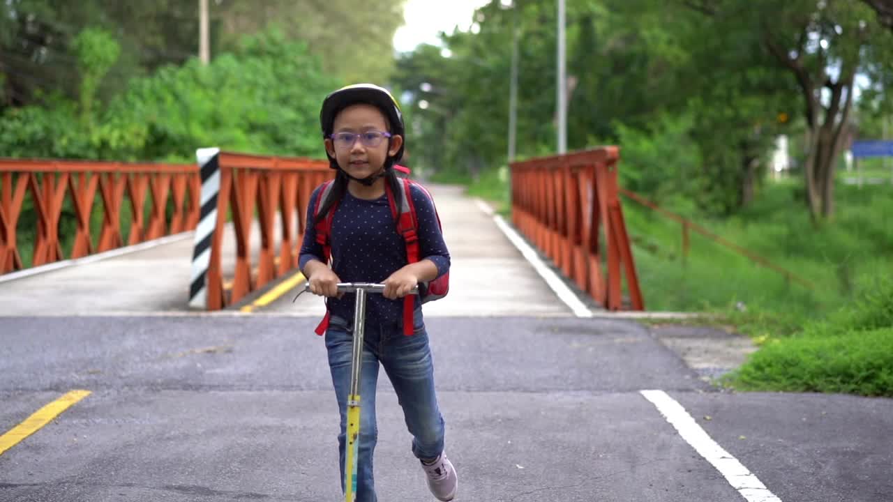 慢动作回到学校。亚洲小女孩背着书包骑着滑板车去上学视频下载