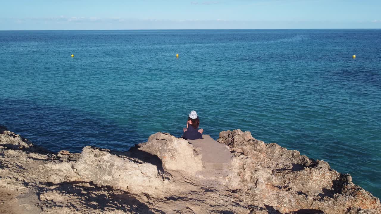 一个女人正坐在海边的一块岩石上视频素材