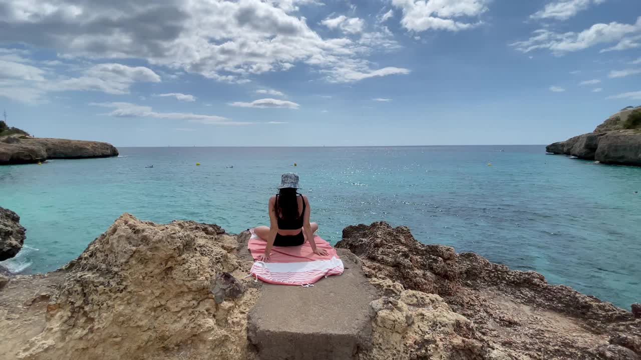 一个女人正坐在海边的一块岩石上视频素材