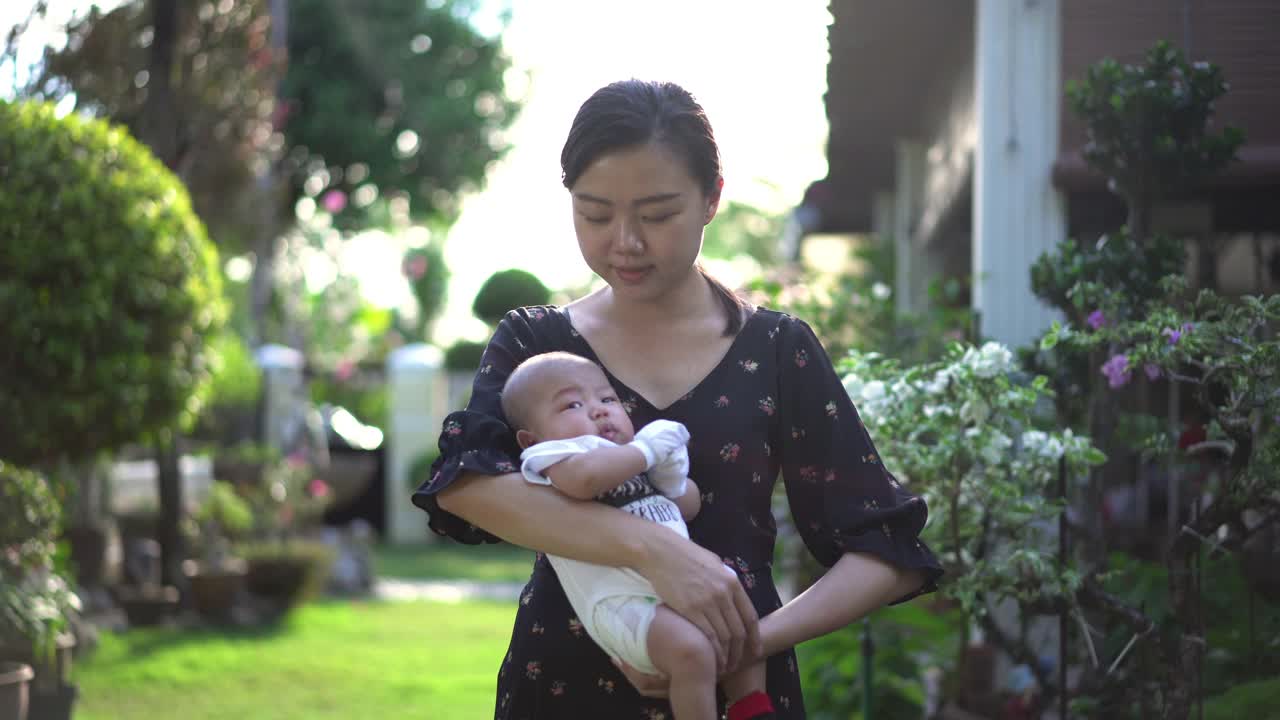 微笑的亚洲妇女抱着她的男婴在后院视频素材