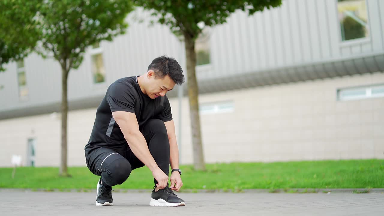 亚洲男运动员跑步准备慢跑，系好鞋带，看起来像个健身追踪器视频素材