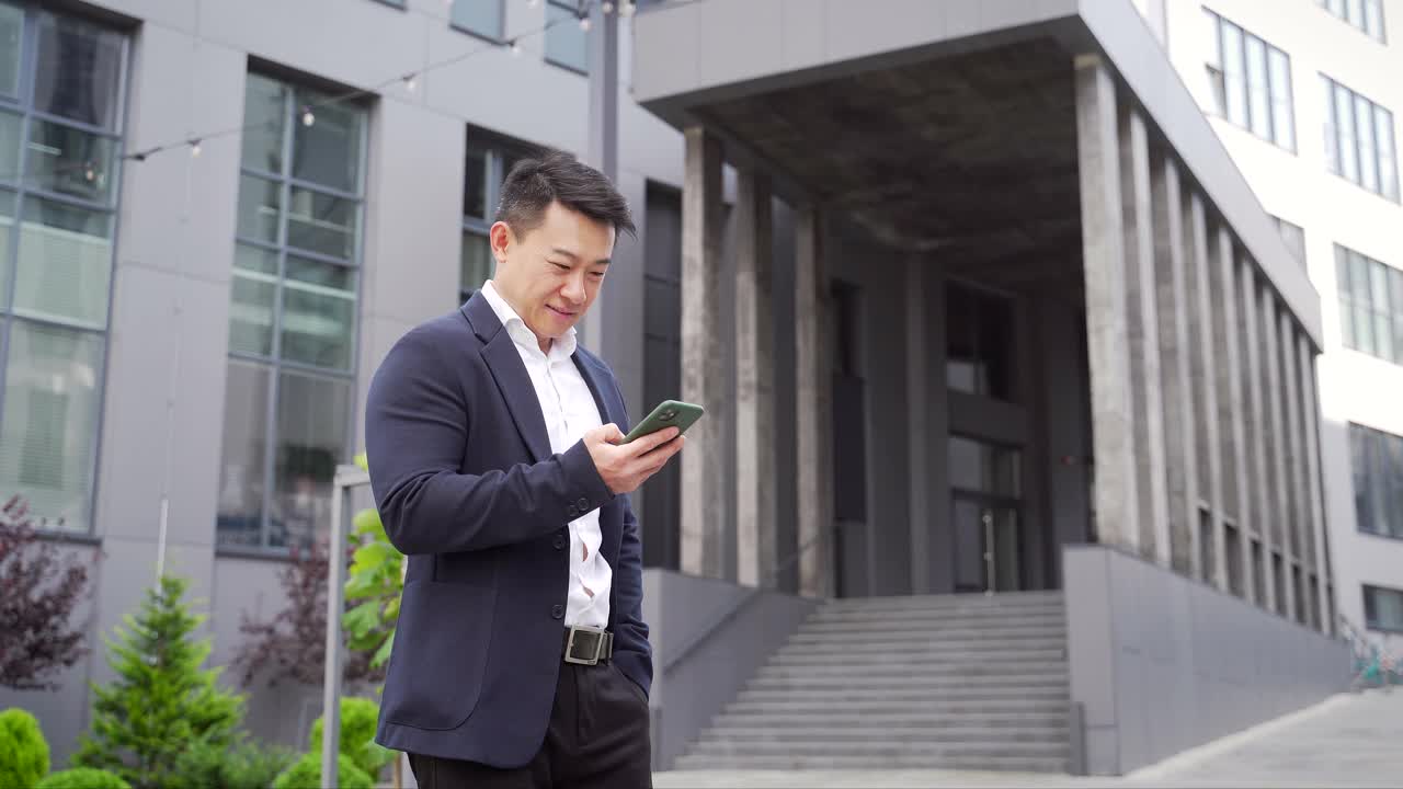 在户外看着智能手机庆祝成功的亚洲商人视频素材