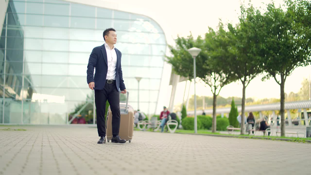 亚洲旅游商人带着行李走在城市背景的公共交通大楼的一条城市街道上视频素材