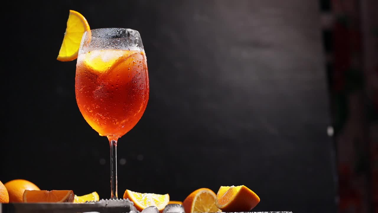 用鸡尾酒勺喷洒Aperol。鸡尾酒aperol与橙片，冰和薄荷。相机在夏日鸡尾酒杯上移动视频素材