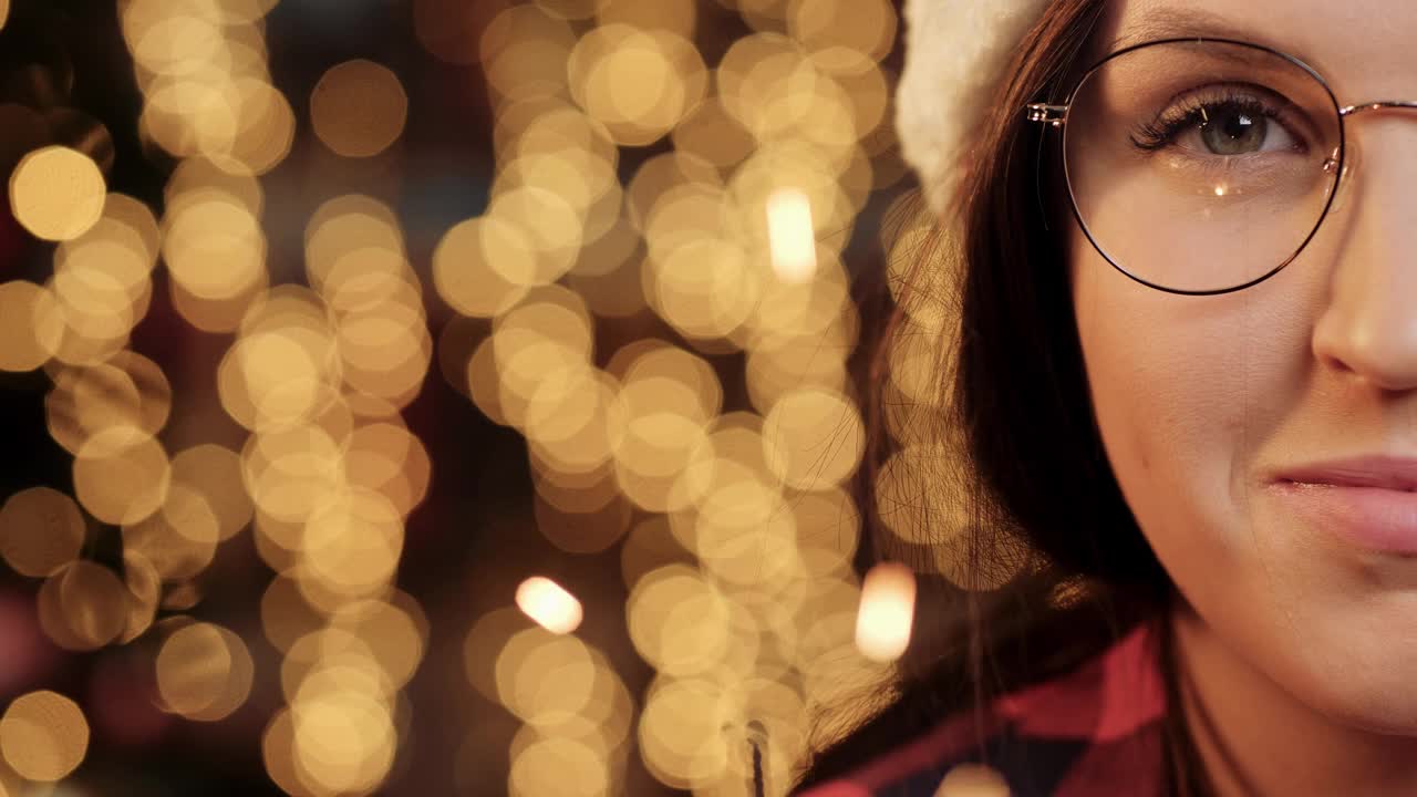 Merry Christmas and Happy New Year text coming up on the background of Christmas lights模糊在bokeh, woman face with glasses looking at the camera and holding a sparkeh。特写镜头视频素材