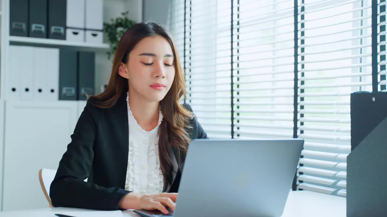 疲惫迷人的亚洲女商人在工作桌上看着许多文件工作。忙碌的女员工由于工作到很晚，在办公室的电脑桌上放着工作文件，感到疲惫头痛视频素材