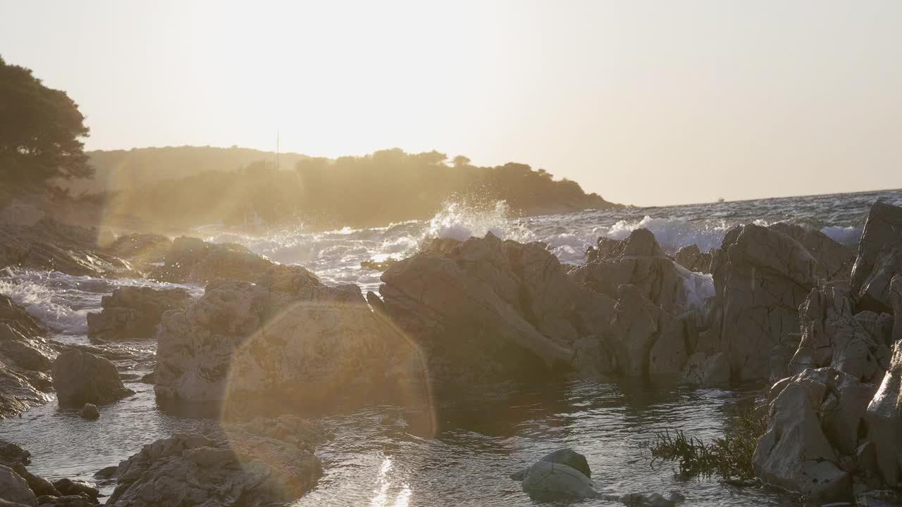 在夕阳的映衬下，海浪拍打着岩石视频素材