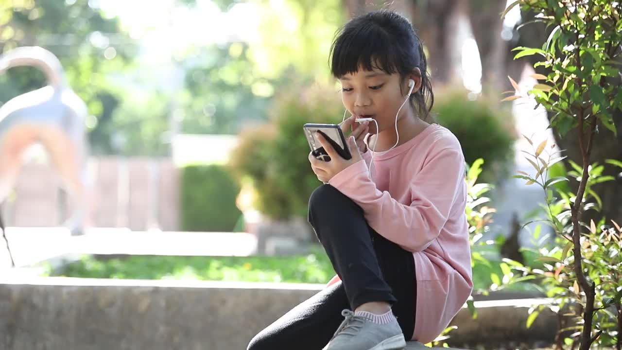 漂亮的亚洲女孩戴着耳机，用手机听音乐视频素材