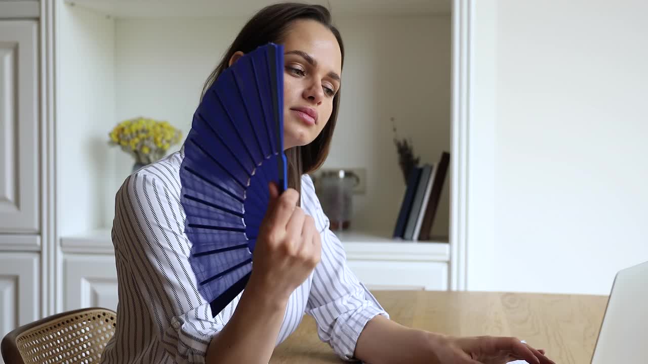 炎炎夏日，一名过热的女子用扇子给自己降温视频素材