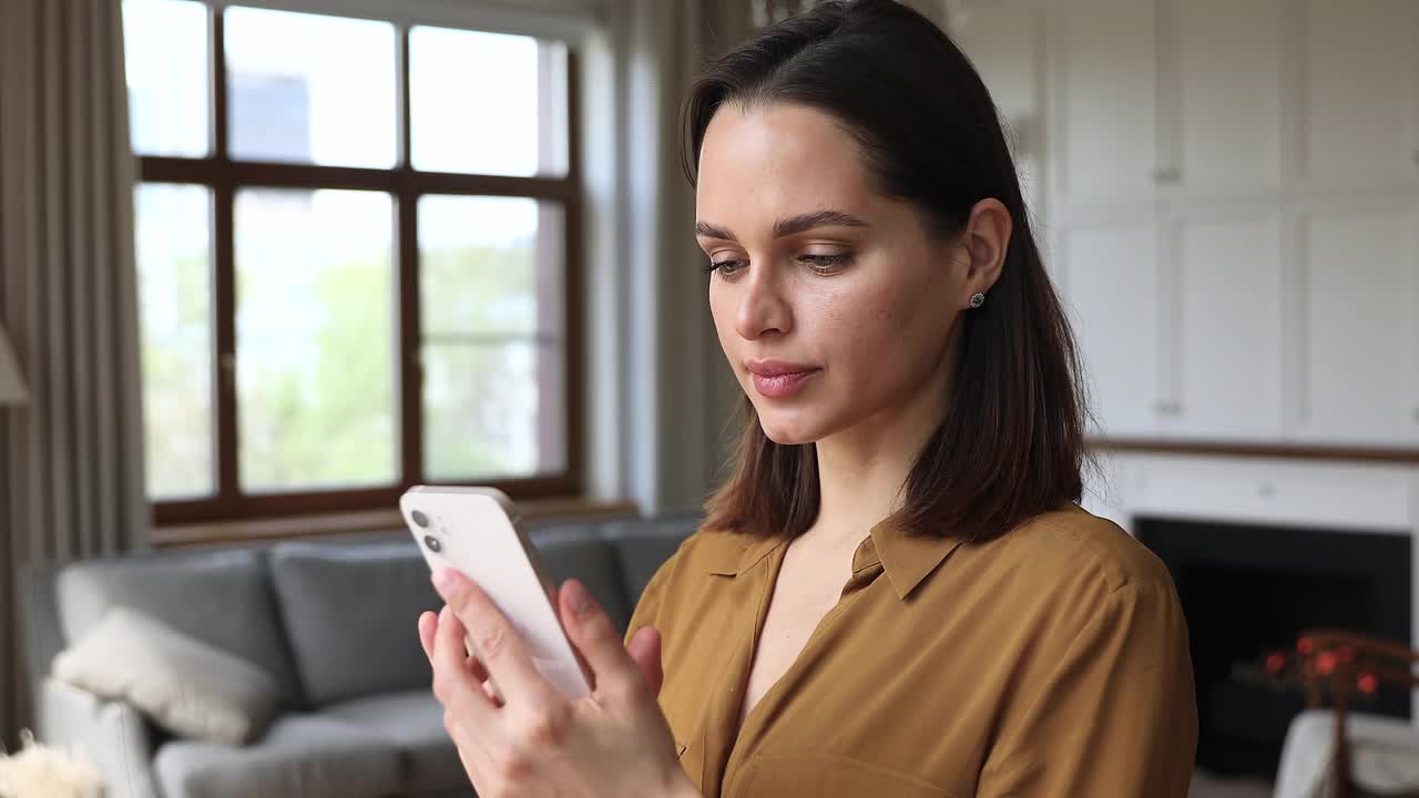 女人站在舒适的客厅里用手机发短信视频素材