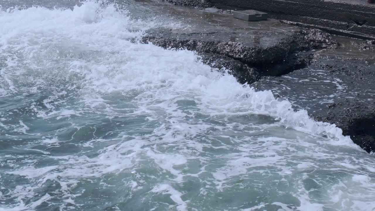 在蓝色的海洋中，波浪拍打着岩石。海浪拍打着空石崖。在溅起白色泡沫的岩石峭壁上坠落视频素材