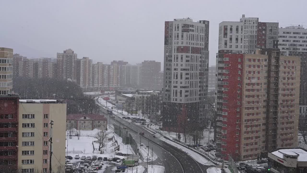 莫斯科，俄罗斯，02.28.2021——冬天的城市景观，漫天飞雪。从高处看城镇的景色。暴风雪在街上飘着雪花。住宅建筑和有汽车行驶的道路视频素材