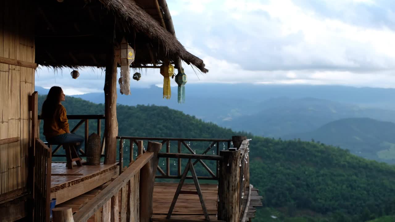 一个女旅行者坐在木屋里，看着美丽的山景视频素材