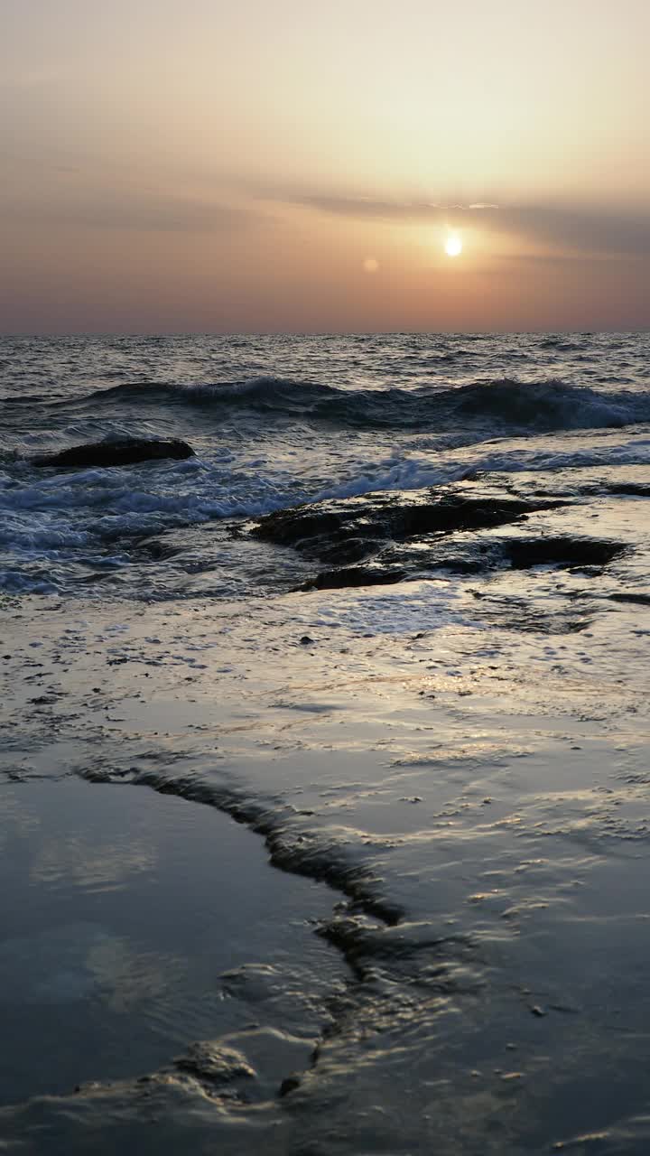 日出时的海岸线景观，太阳在地平线上，海浪拍打着海岸。视频素材