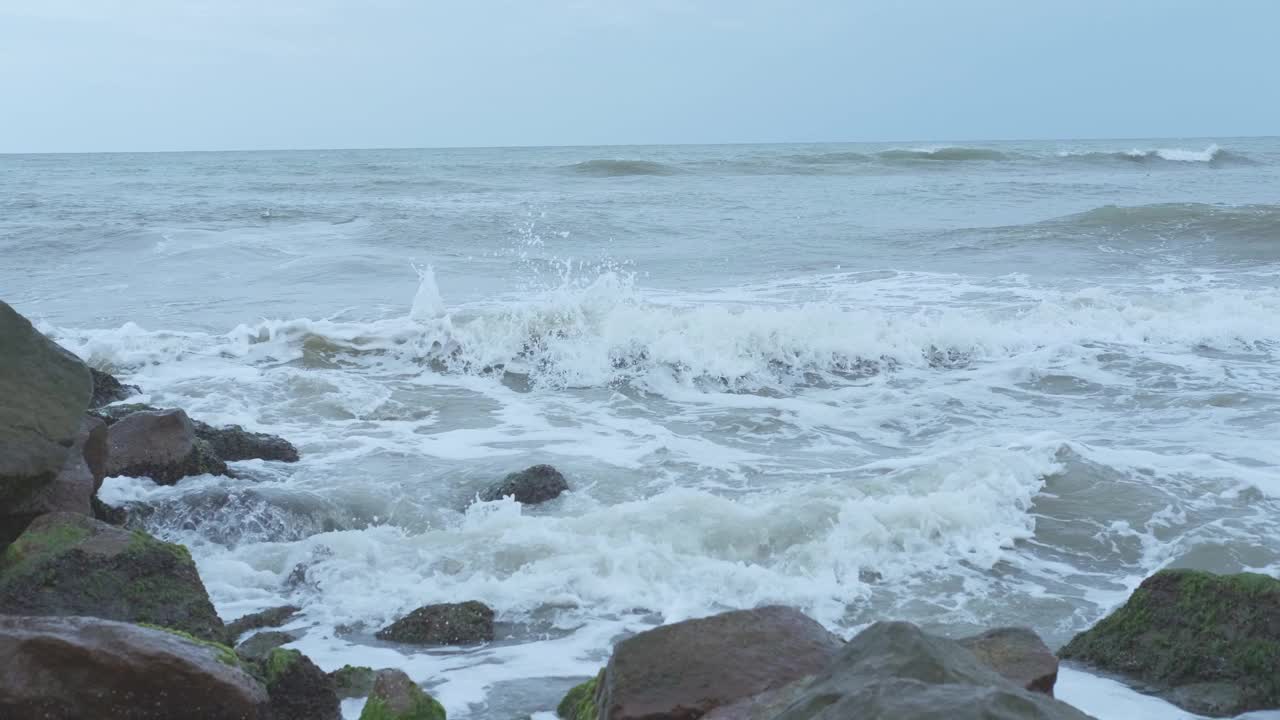 在多云的日子里，海浪挤压着海岸的巨石视频素材