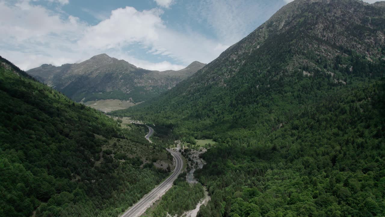 美丽的无人机视野的沥青公路在高山上。山脉消失在天空中，天空有些许阴云，但山峰被阳光照亮。视频素材