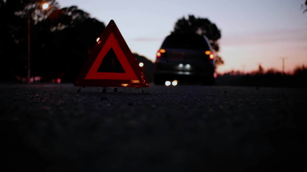 夜里，一辆失灵的汽车开着警报器停在路边。在汽车后面的路上有一个紧急停车标志。视频素材