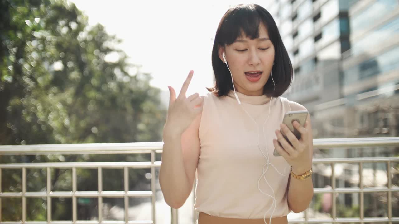 跳舞的亚洲女人用智能手机欣赏音乐视频素材