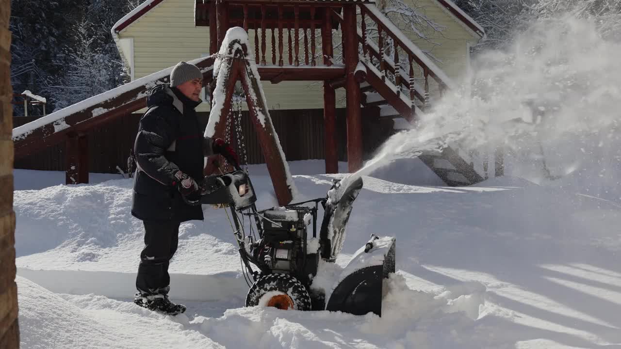 有人用吹雪机清扫人行道上的积雪。暴风雪过后，冬日阳光明媚的乡间小屋。视频素材