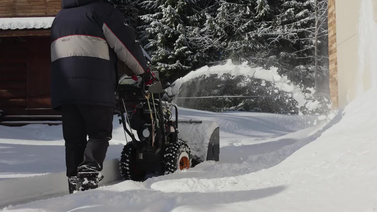 有人用吹雪机清扫人行道上的积雪。暴风雪过后，冬日阳光明媚的乡间小屋。视频素材