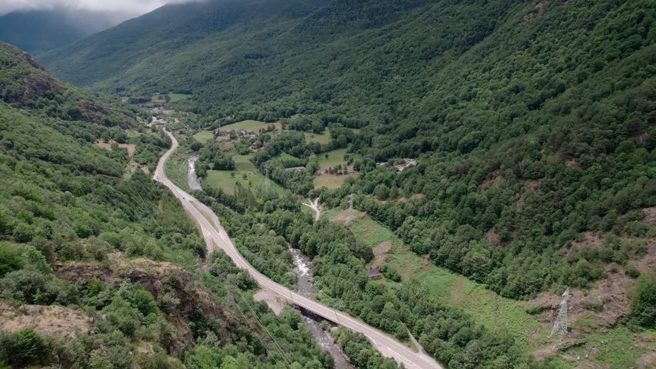 美丽的无人机视野的沥青公路在高山上。山脉消失在天空中，天空有些许阴云，但山峰被阳光照亮。视频素材