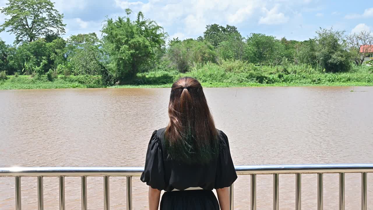 一个年轻的亚洲女子举起双臂，欣赏着流经泰国清莱省的Kok河的美丽景色。视频素材