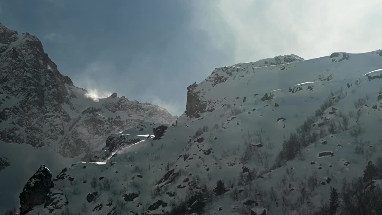 风把雪吹下了悬崖。在阳光明媚的日子里，高高的雪山。缩小视频素材