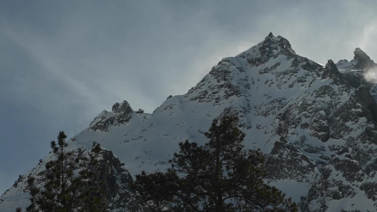 在长焦镜头上的时间流逝，高山的雪峰被风吹起的雪。山区恶劣的天气条件视频素材