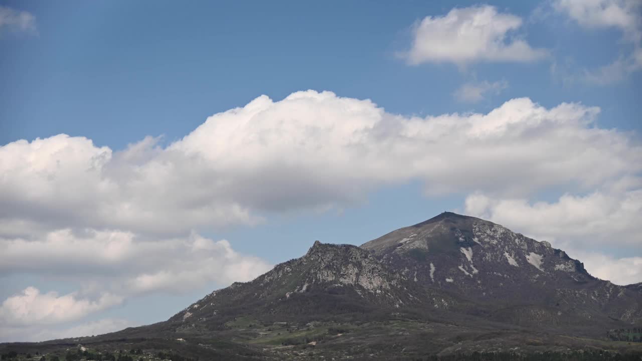 夏日的白天，在一座有几座山峰的山上，云朵飘浮，在绿色的森林里投下阴影。视频素材