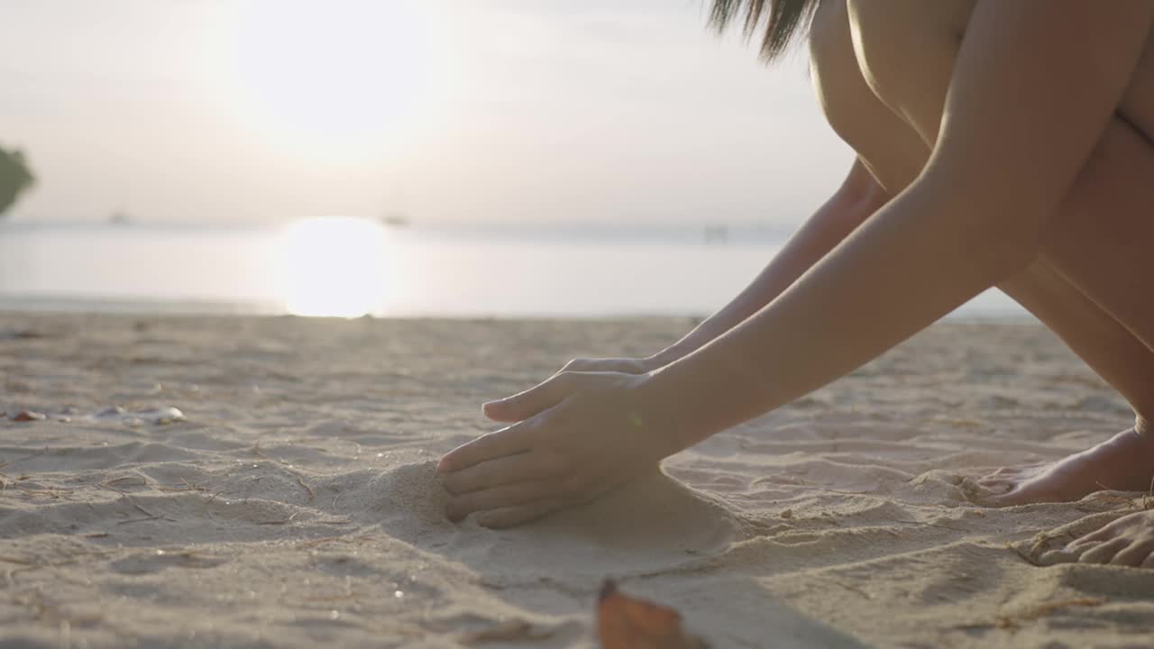 无忧无虑的女孩在暑假度假时，坐在热带海滩上的沙滩上，慢动作视频素材