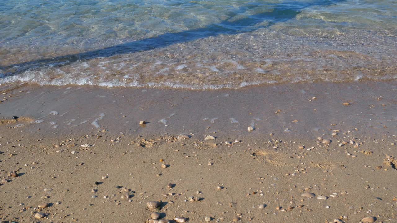 女孩与苗条的腿走在海浪在海边。美丽的绿松石水在夏天的海滩。放松和旅行，度假的概念。温暖的阳光视频素材