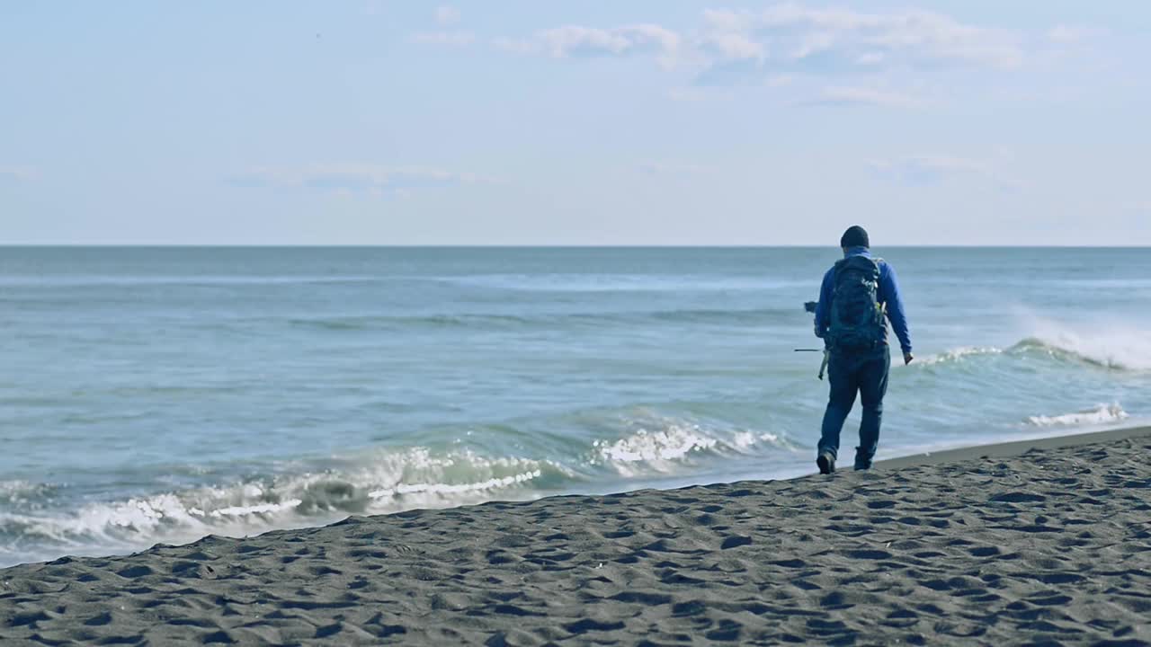 一名男子在阳光明媚的户外海滩上散步拍照。Avki视频素材